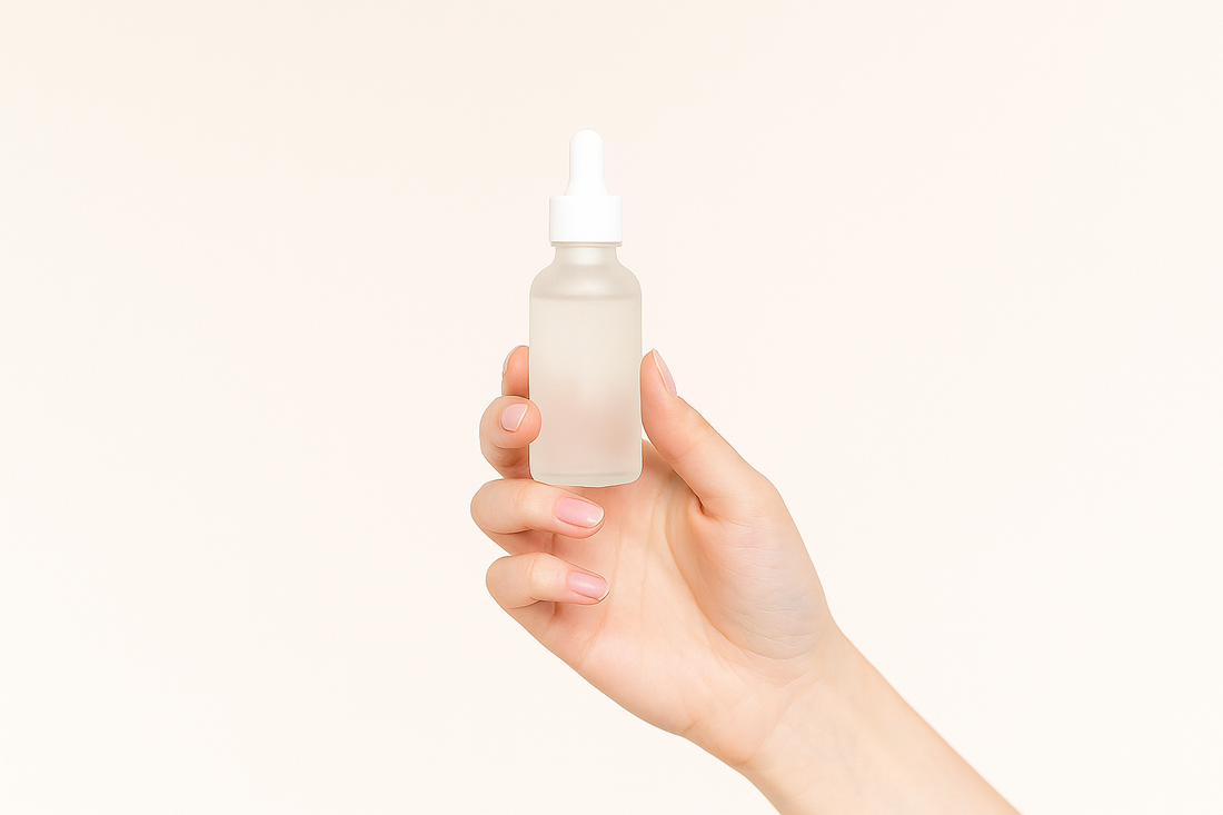 Hand einer Frau hält eine transparente Serumflasche vor einem hellen, neutralen Hintergrund.