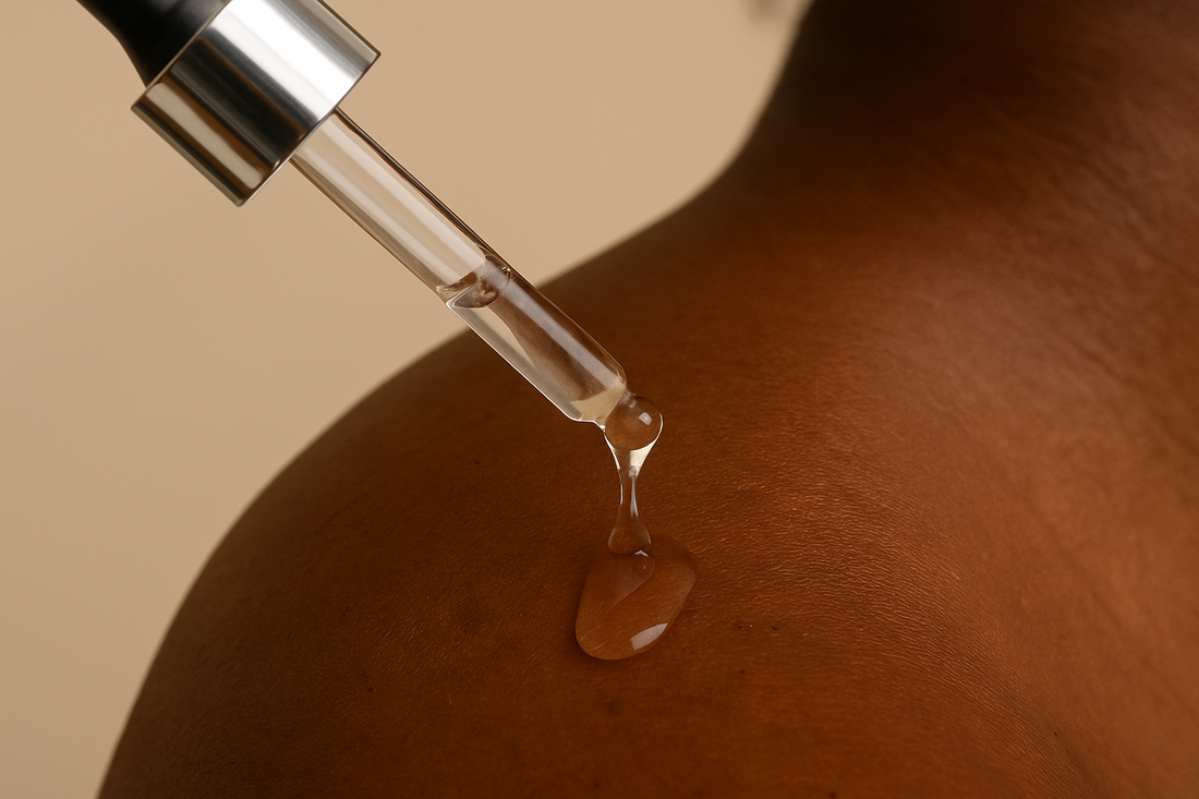 Nahaufnahme eines Serums, das aus einer Pipette auf dunkle Haut tropft; warme Beleuchtung, ästhetisches Haut- und Produktdetail.